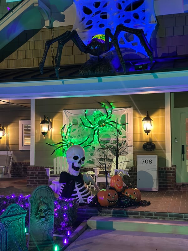 Front porch at night with a giant spider, skeleton, pumpkins, and purple lights
